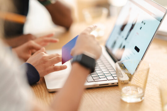 Two people are making an online purchase. One hand holds a card, pointing at the laptop screen, .They are browsing an e-commerce site, showcasing digital payment