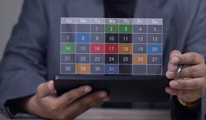 A businessman holds a tablet and pen, using a digital calendar app to schedule appointments, plan events, and mark important deadlines on a colorful planner interface.