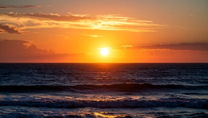 A stunning coastal vista showcasing a fiery sunset over the ocean's expanse, with clouds reflecting the golden light