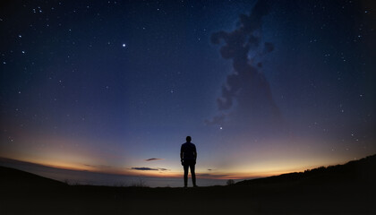 Fototapeta premium Man standing in silhouette under starry night sky at dusk 