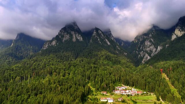 Tops of the mountains are hidden by the dramatic cloudscape. Evergreen pine tree woods cover the slopes of the rocks. The Bucegi Mountains of the Southern Carpathians, Romania.
