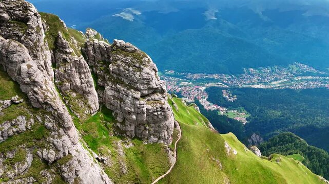Grey cliffs covered with green grass. Spectacular scenery of the village at the mountain foot. The Bucegi Mountains, Romania.