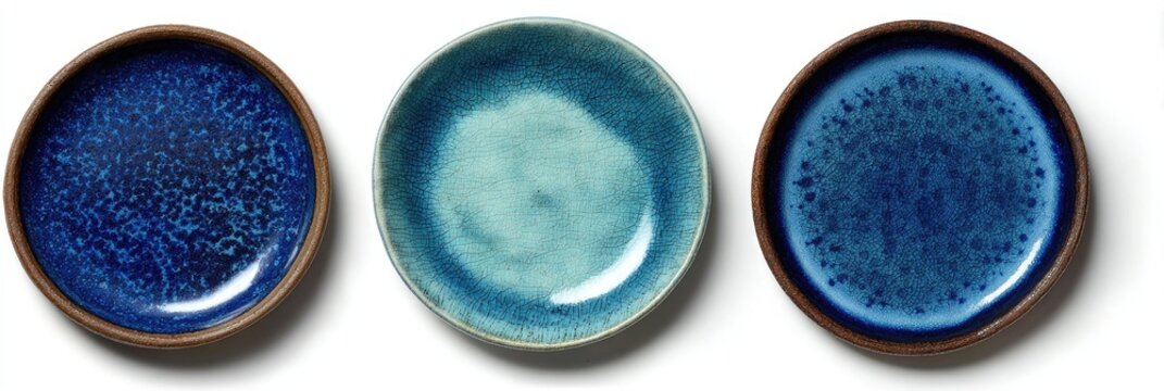 Three round ceramic plates in varying shades of blue, with a mottled or speckled glaze, resting on a white background.  The plates have a dark brown rim - Powered by Adobe