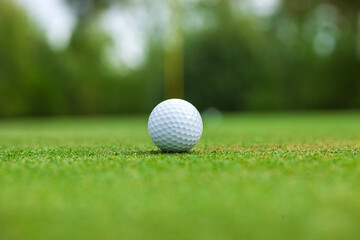 Low angle selective focus view of a golf ball on a green with the flag stick behind