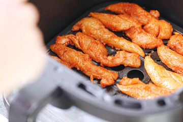 Raw marinated chicken tenderloins placed in modern air fryer. Fresh poultry meat ready for baking. Homemade cooking preparation. Domestic kitchen appliance. Healthy alternative to traditional frying.
