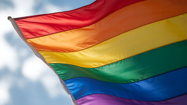 Rainbow flag waving in the wind against a cloudy sky