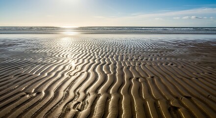 Expansive view of rippled sand patterns on a beach at low tide with sunlight reflecting on the water.