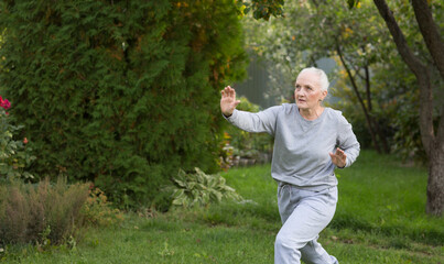 senior woman practice Tai Chi Chuanand yoga in the garden near the house on a summer day.  