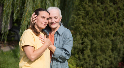 an elderly woman hugs her adult daughter near the house in the garden. Deep conversation. emotional intimacy. support in two age generations