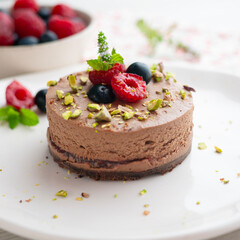Chocolate mousse tart filled with jam and decorated with pistachios and red berries.