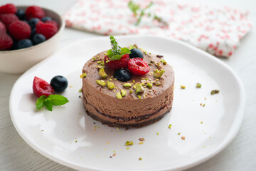 Chocolate mousse tart filled with jam and decorated with pistachios and red berries.