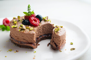 Chocolate mousse tart filled with jam and decorated with pistachios and red berries.