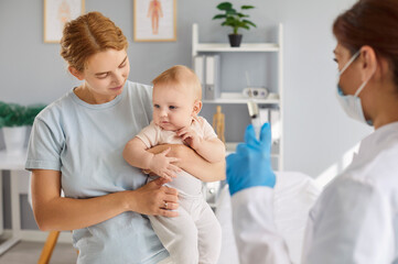 Mom holds cute 6 or 7 month old baby son or daughter for nurse practitioner to give flu, covid19, polio, hepatitis, diphtheria or tetanus inoculation jab. Child vaccination, illness prevention concept