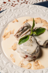 Close-up view of round pieces of meat with white sauce and a stylized leaf.