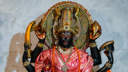 A colorful Hindu goddess statue featuring a dark-skinned deity with multiple arms, wearing a pink...
