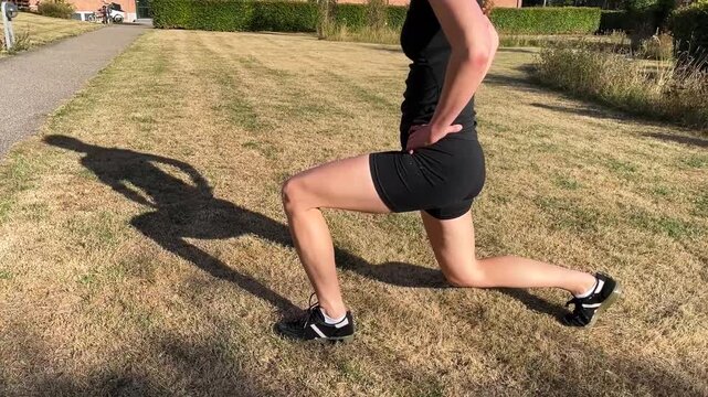 Fit young woman exercising outdoors on a grass field in the sun