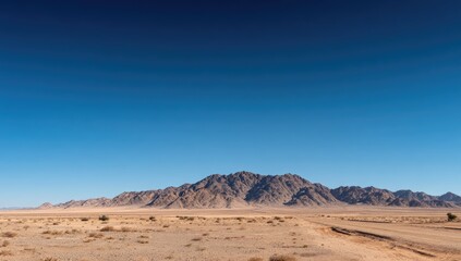 Expansive desert landscape with rugged mountains under a clear blue sky.