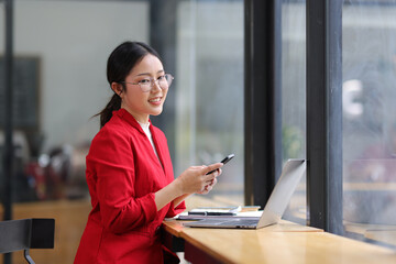 Obraz premium Asian business woman wearing glasses Smiling and happy sitting Working with laptop at desk in office