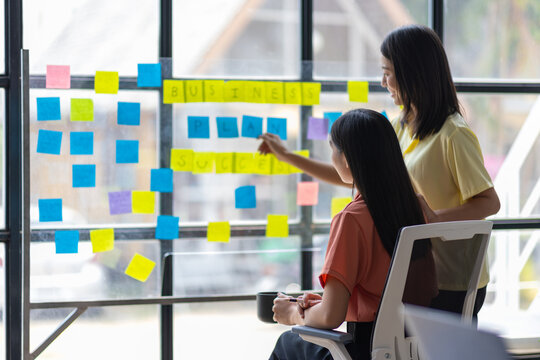Colleagues and thoughtful businesswoman thinking creatively and drafting initial business planning with paper stickers on a transparent board. Strategy analysis and business planning.