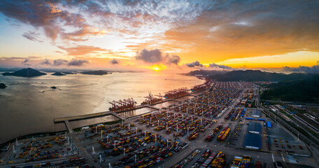 Panoramic view of a massive industrial container port and cargo ship terminal against a beautiful dramatic sunset sky.