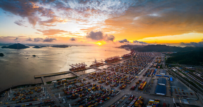 Panoramic view of a massive industrial container port and cargo ship terminal against a beautiful dramatic sunset sky.