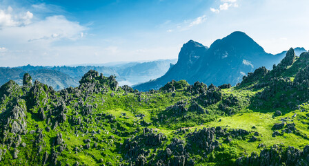 Obraz premium Beautiful scenic landscape of lush green karst mountains and dramatic rocky peaks under a clear blue sky on a sunny day.