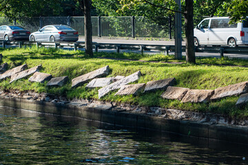 Naklejka premium Granite embankment restoration on riverbank with planned replacement of stone slabs to stabilize shoreline. Erosion control at water edge, engineered support for soil retention, long term maintenance 