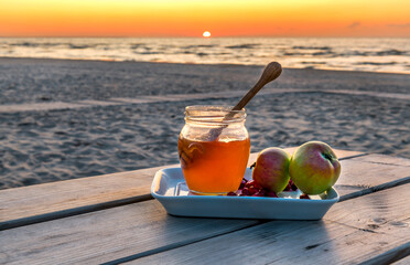 Festive food, background with blurred sun, sand e beach and waving  sea. Honey and apple are traditional food attributes for Jewish New Year holiday - Rosh Hashanah
