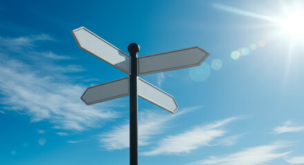 A blank directional signpost stands against a bright blue sky with wispy clouds and a shining sun.