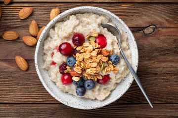 Oatmeal porridge with berries and muesli on wooden table background, top view