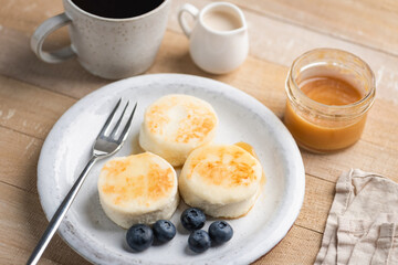 Cottage cheese fritters aka Syrniki served with caramel sauce and blueberries. Healthy fried cheese pancakes rich in calcium and protein