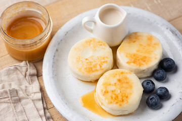 Cottage cheese fritters aka Syrniki served with caramel sauce and blueberries. Healthy fried cheese pancakes rich in calcium and protein