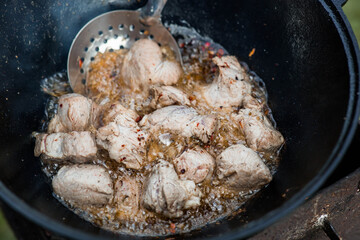 Cooking recipe for cooking meat in a cast-iron cauldron outdoors. Cooking food. Frying meat.