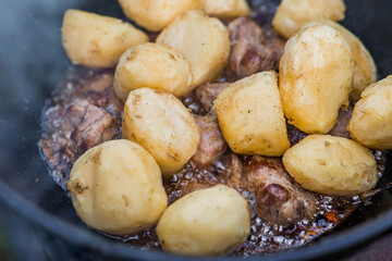 Cooking recipe for cooking meat with potatoes in a cast-iron cauldron outdoors. Cooking food. Frying meat.