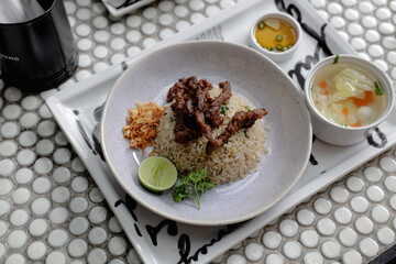 Top view Paradise beef fried rice served with grilled beef slices, lime, parsley, and crispy shallots. Comes with clear soup and dipping sauce on the side.