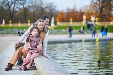 Fototapeta premium Happy family of three, father, mother and daughter enjoying family time together in Luxembourg garden of Paris, France.