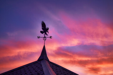 A weather vane in the form of an eagle and indicating the cardinal directions is installed on the roof of the building, dawn has just begun, the first rays have colored the sky, a very beautiful