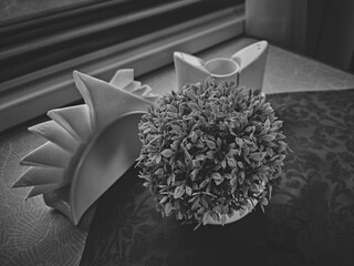 In a cheap eatery, there is a pot of artificial flowers and napkins on the table, a black and white still life with napkins and flowers