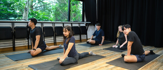 Group of young adults performing seated pigeon pose on yoga mats inside a bright studio