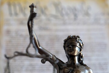 Lady Justice bronze statue and US Constitution blurred page close up. Lawsuit and punishment