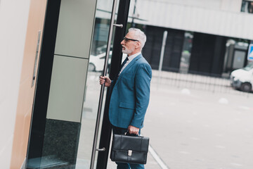 Mature business professional in formal attire entering office building with briefcase showcasing confidence and professionalism