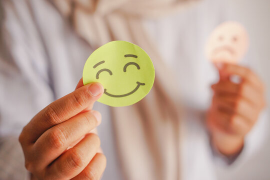 Selective focus of female hands holding happy and angry face paper emoticons . Feedback rating, emotional intelligence, balance emotion control, mental health assessment, bipolar disorder concept