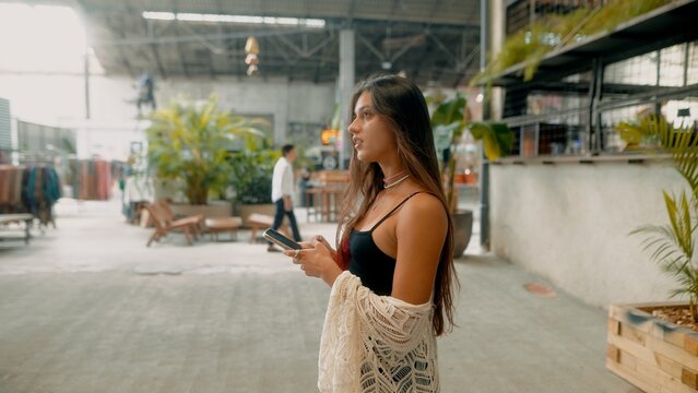 A Young Woman Posing Gracefully in a Vibrant Modern Urban Space While Using Her Smartphone