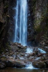 A powerful waterfall plunges over rugged rocks, creating mist and frothy splashes. Moss-covered stones at the base add texture and contrast to the dynamic motion of cascading water