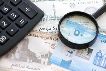 United Arab Emirates dirham currency money bills and calculator with magnifying glass close up. The concept of taxation and money count