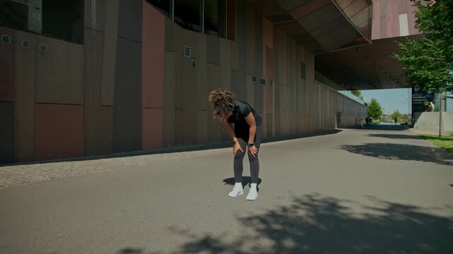A woman wearing headphones stops jogging around the city, looks at her watch and continues her workout.
