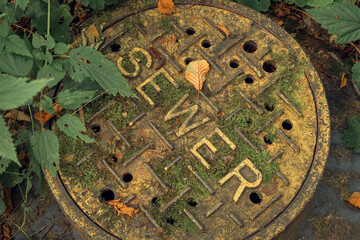 Old Sewer manhole cover covered in moss and leaves