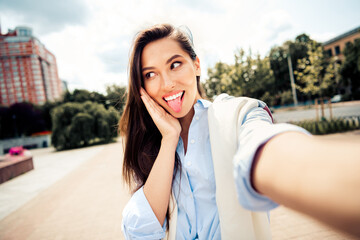 Fototapeta premium Playful young woman takes a fun outdoor selfie in a stylish casual outfit on a sunny day in a city street.