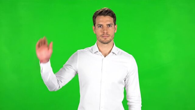 Confident young businessman waving a friendly greeting on a vibrant green screen background, ideal for compositing into diverse professional or casual video projects