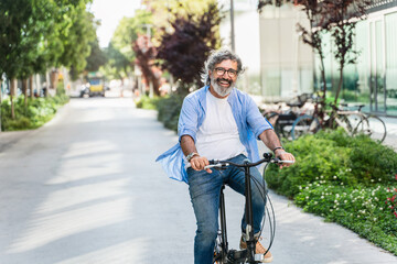 Happy senior man riding bicycle in urban street during sunny day. Positive and healthy retirement